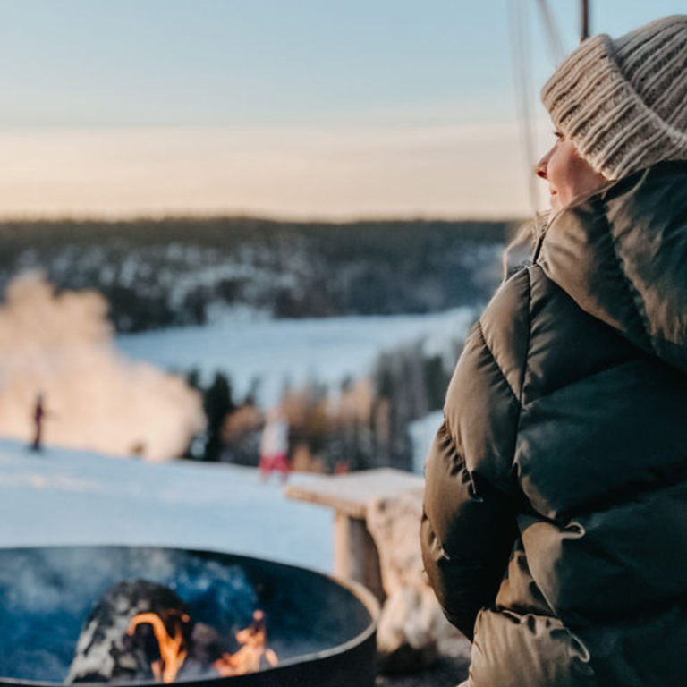 Woman sitting by fire with a view to skiing slopes