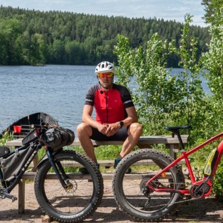 Mies istuu penkillä metsäisen järven rannalla kaksi fatbike-pyörää edessään.