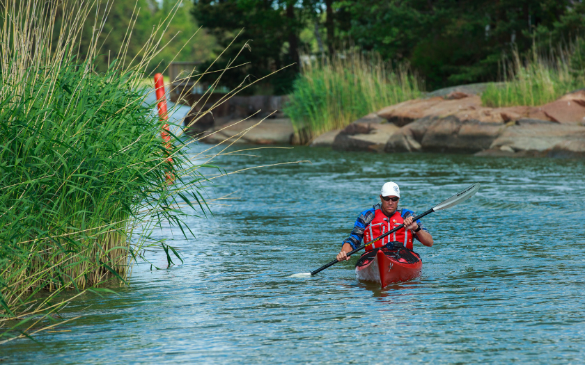 Man kayaking on water with green landscape around.