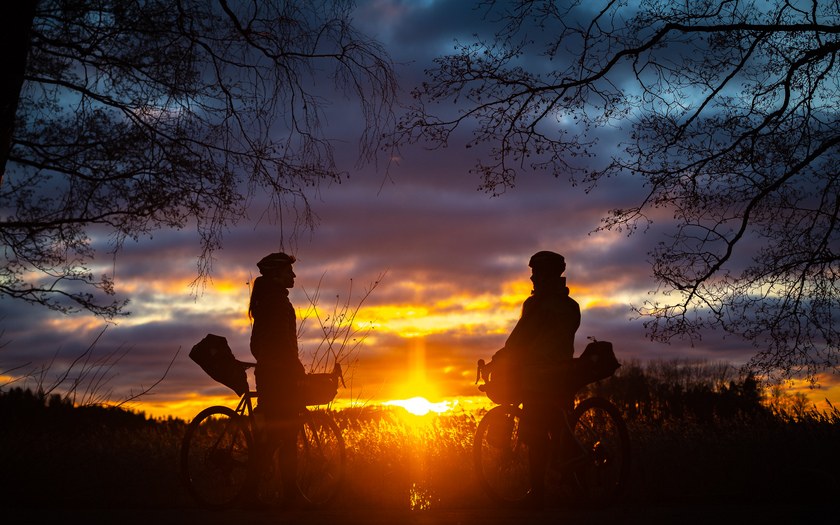 Tunnelmallinen iltavalaistus auringonlaskussa ja kuvassa näkyvät kahden pyöräilijän hahmot.