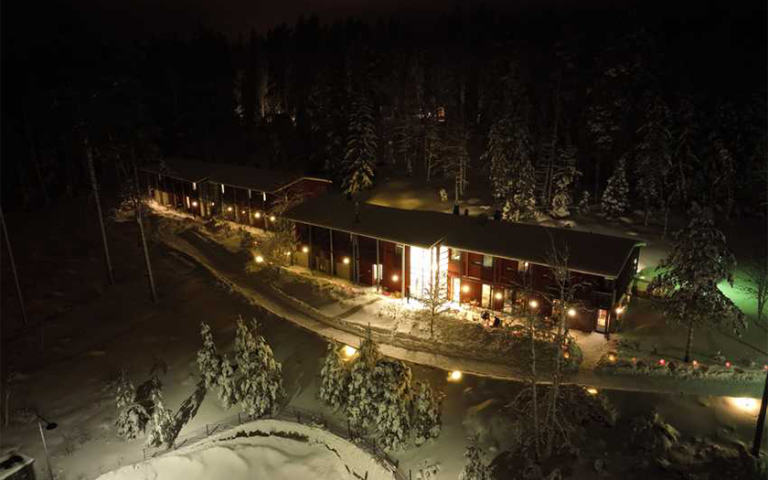 Haltia Lake Lodge hotellirakennus ilmasta käsin kuvattuna talvella iltahämärässä.