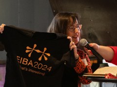 Rebecca Piekkari holding a black t-shirt with the name of the EIBA 2024 congress.