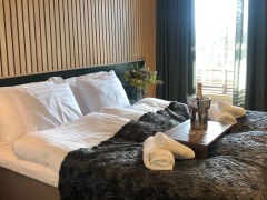 A double bed with towels on the bed and sparkling wine on a tray in a cooler and two glasses.