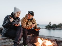 A woman and a man sitting by a campfire and eating